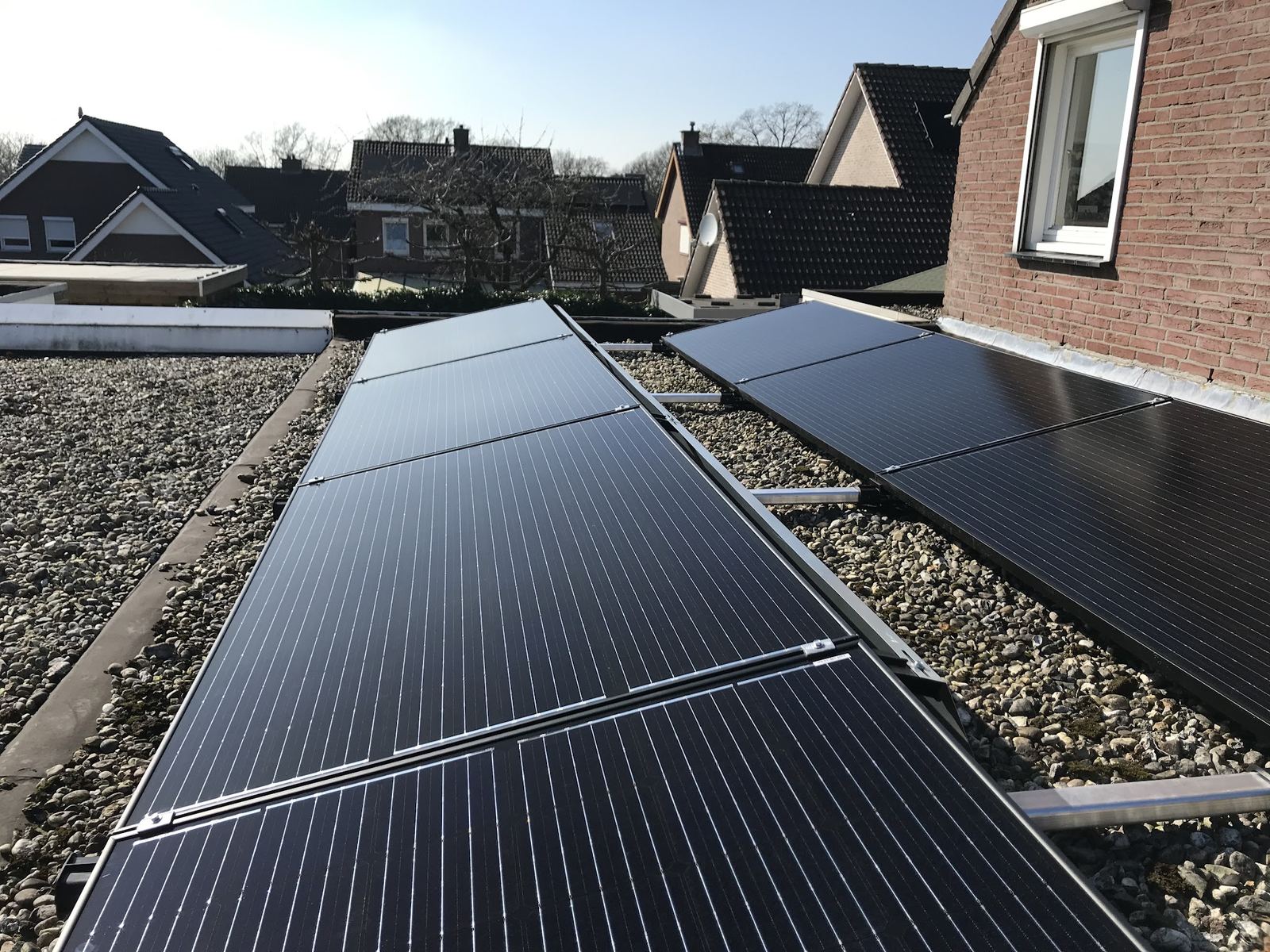 Zwarte zonnepanelen op een plat grinddak in een woonwijk