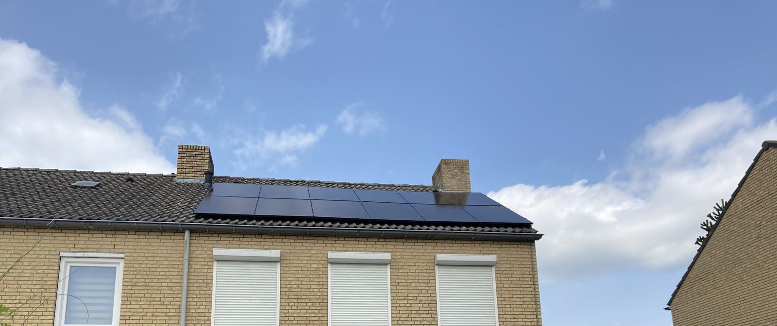 Rij zwarte zonnepanelen op het dak van een woning onder een blauwe lucht