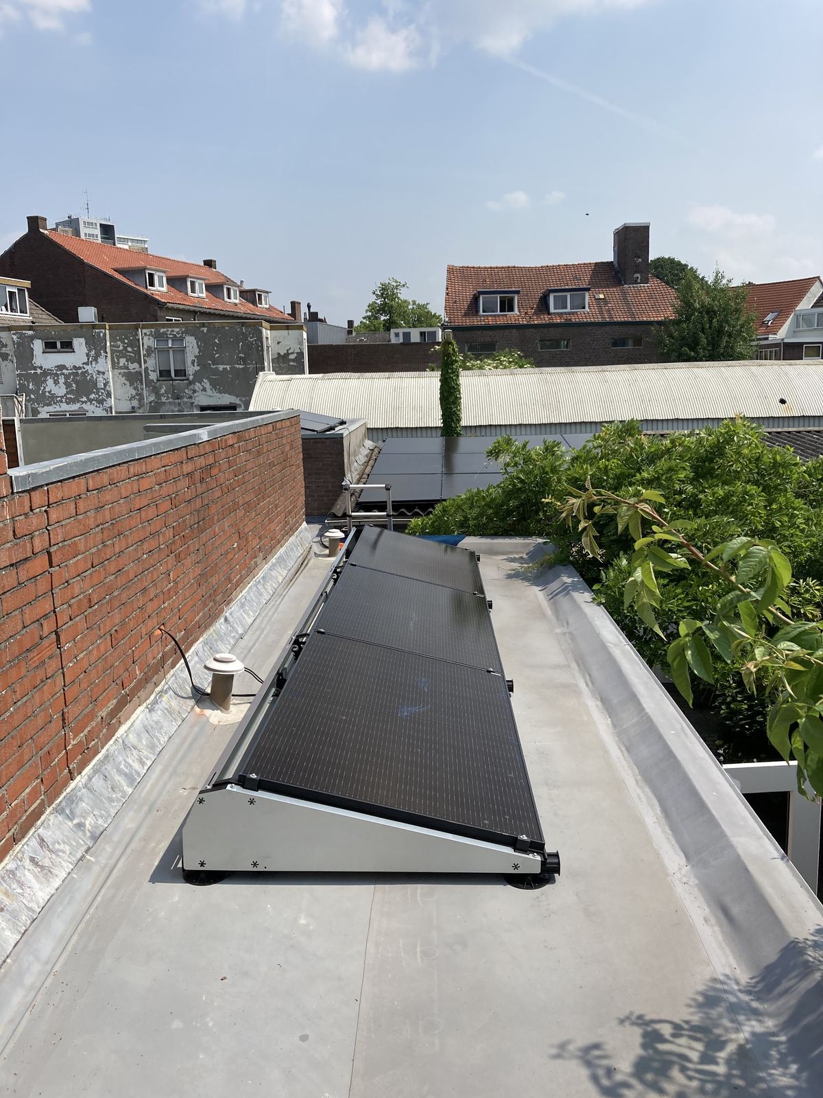 Schuin opgestelde zonnepanelen op een smal plat dak tussen stadswoningen