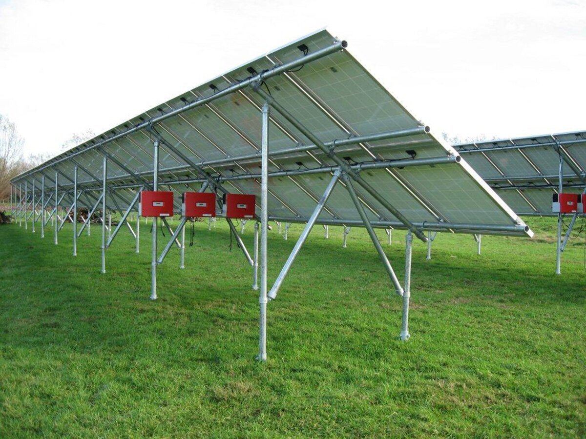 Veldopstelling van zonnepanelen in een weiland met rode omvormers
