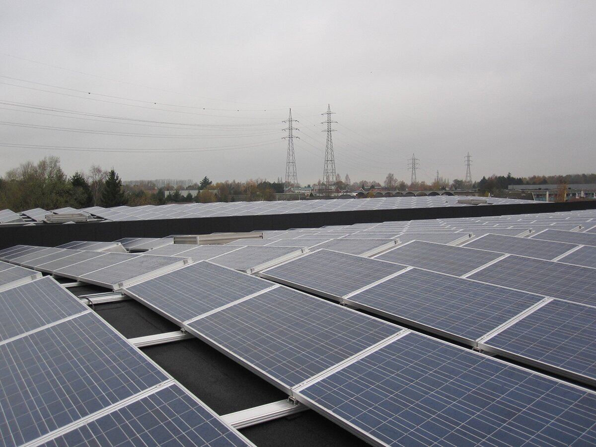 Zonnepanelen op een groot plat dak met hoogspanningsmasten in de verte